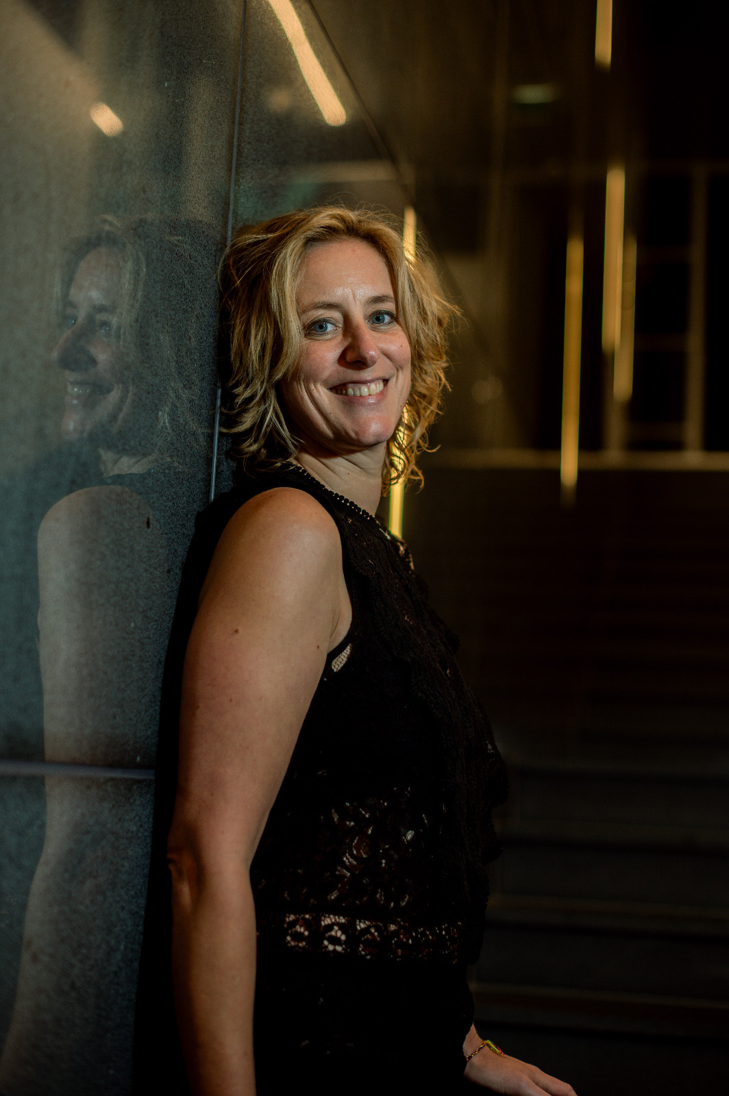 Self-love coach and trauma-informed facilitator smiling confidently in a black lace top, standing against a reflective wall — expert in embodied healing and nervous system regulation.